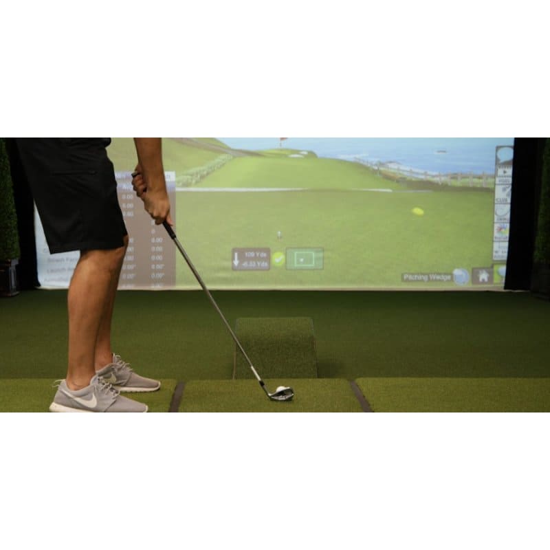 Person playing golf on a simulator with a screen displaying a golf course.